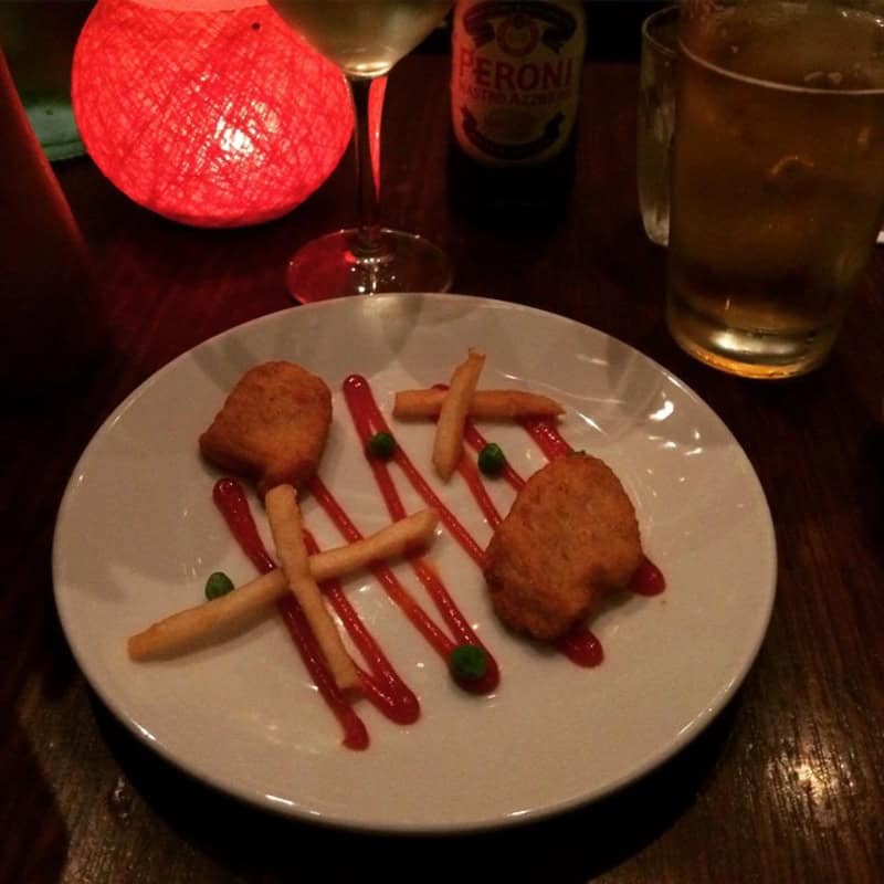 Two fried appetizers with sauce and vegetables on a white plate at a restaurant.