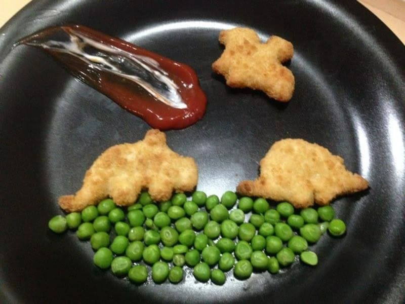 Fish-shaped fried food with green peas and ketchup on a black plate.