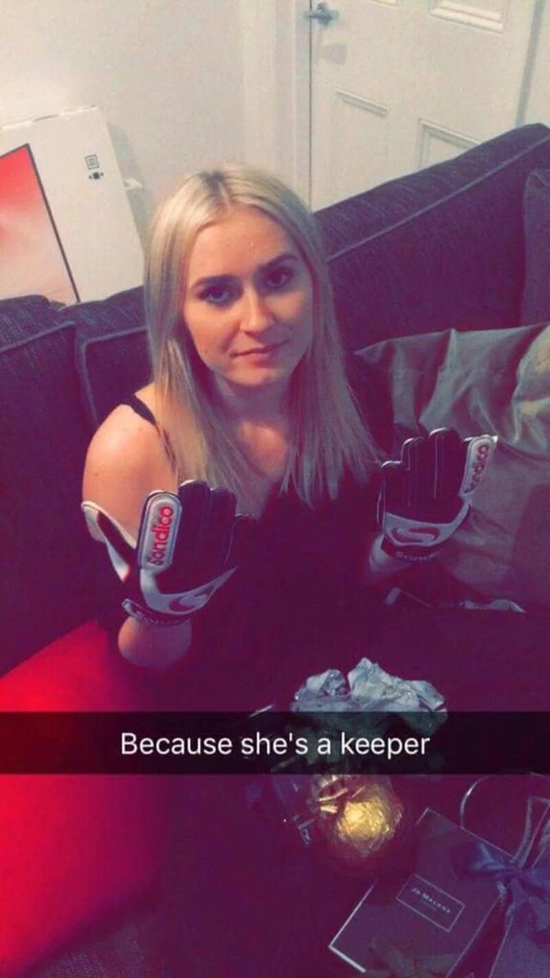 A woman with blonde hair wearing black gloves sitting on a dark couch.