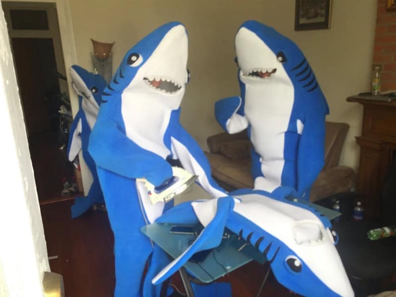 Shark costumes with children playing and sitting on a shark inflatable in a living room.