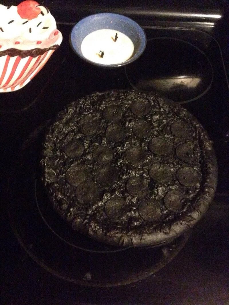 Charcoal pizza on a black baking stone with a cupcake and candle in the background.