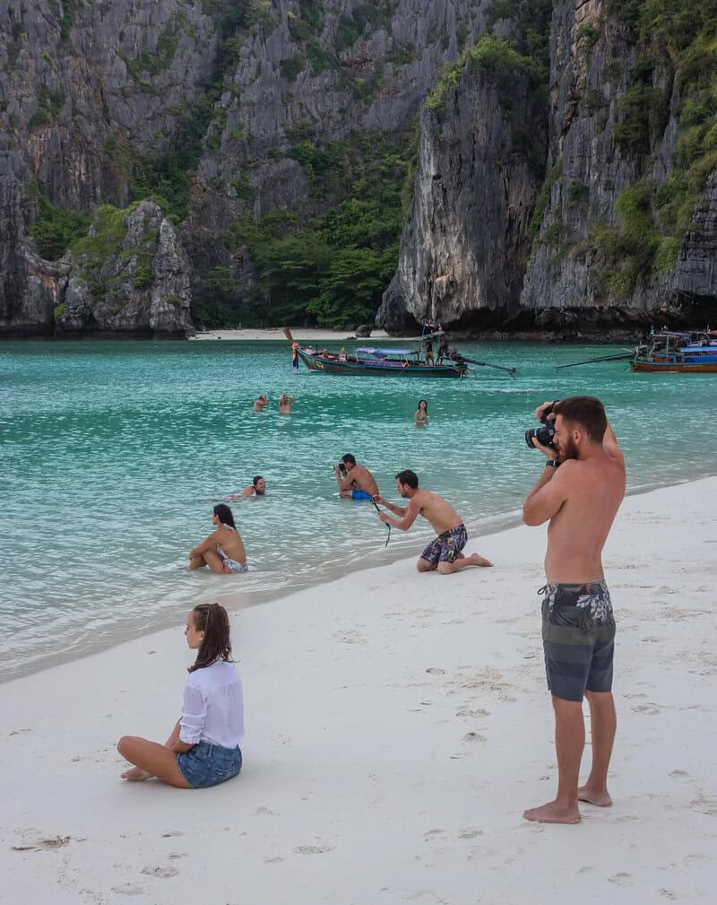 People enjoying a beach with turquoise water and limestone cliffs in the background.