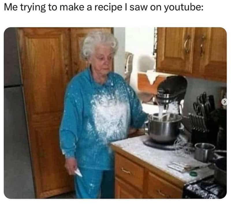A woman with white hair wearing a blue outfit covered in flour in a kitchen.