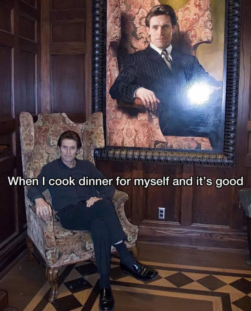Man sitting in a vintage armchair with a large portrait of a man in a suit behind him.