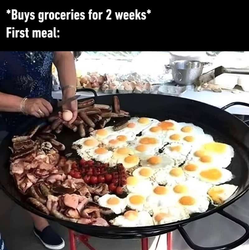 Large pan with eggs, bacon, sausages, and tomatoes, with a person cooking.