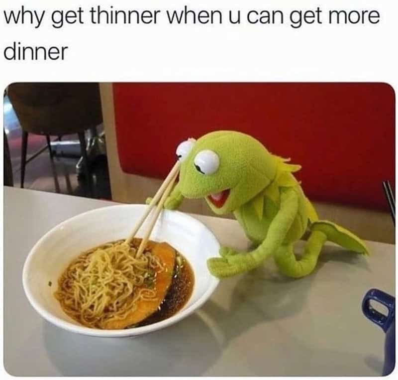 Kermit the Frog plush toy eating noodles with chopsticks at a table.