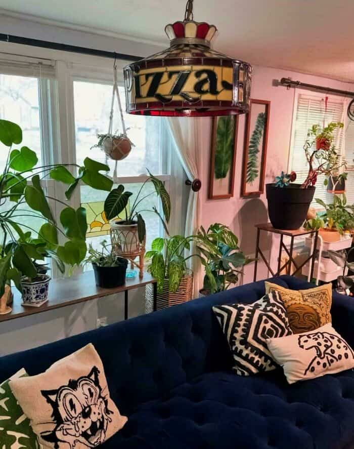 Zaza lamp hanging above a blue sofa with patterned pillows, surrounded by houseplants and framed art.