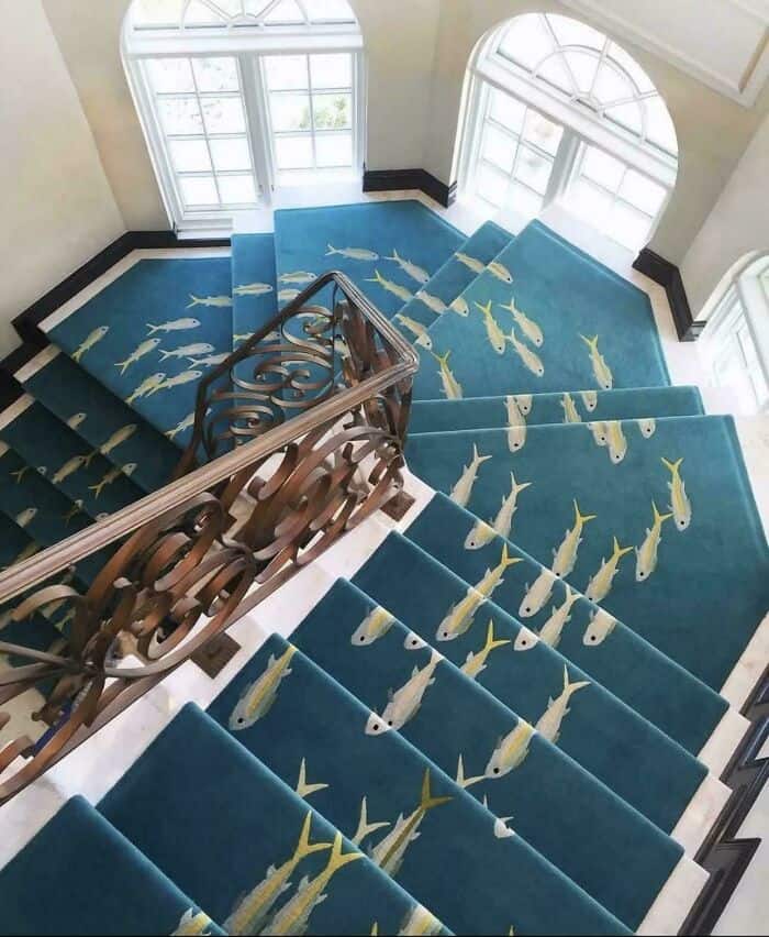 Blue staircase carpet with yellow fish pattern and large arched windows.