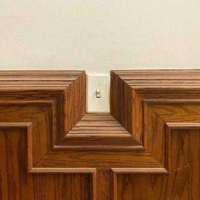 Wooden corner with electrical outlet and wall paneling.
