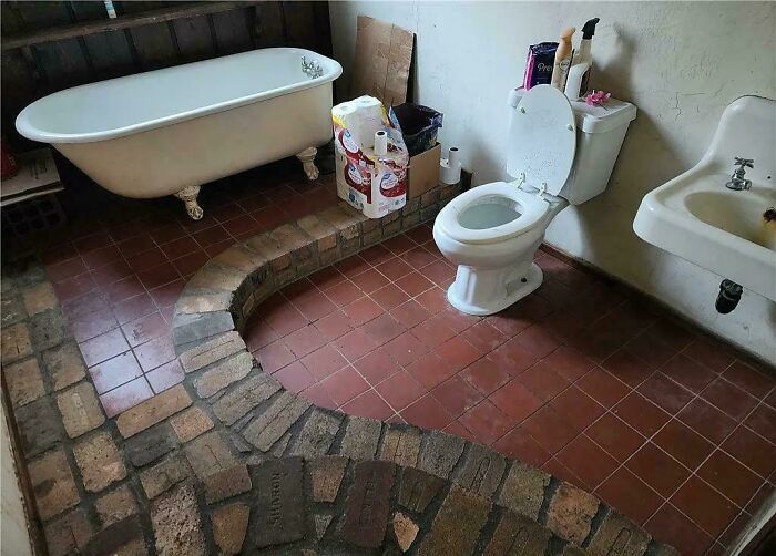 Bathroom with a clawfoot tub, toilet, and sink, featuring a brick pathway on the floor.