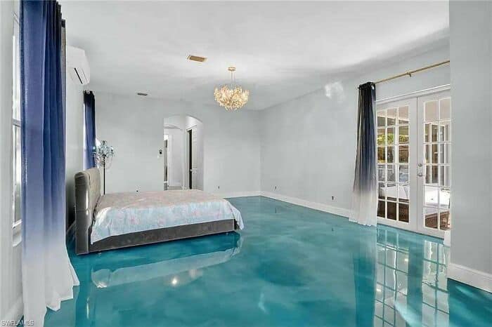 Luxury bedroom with blue flooring, white walls, large windows, and elegant chandelier.