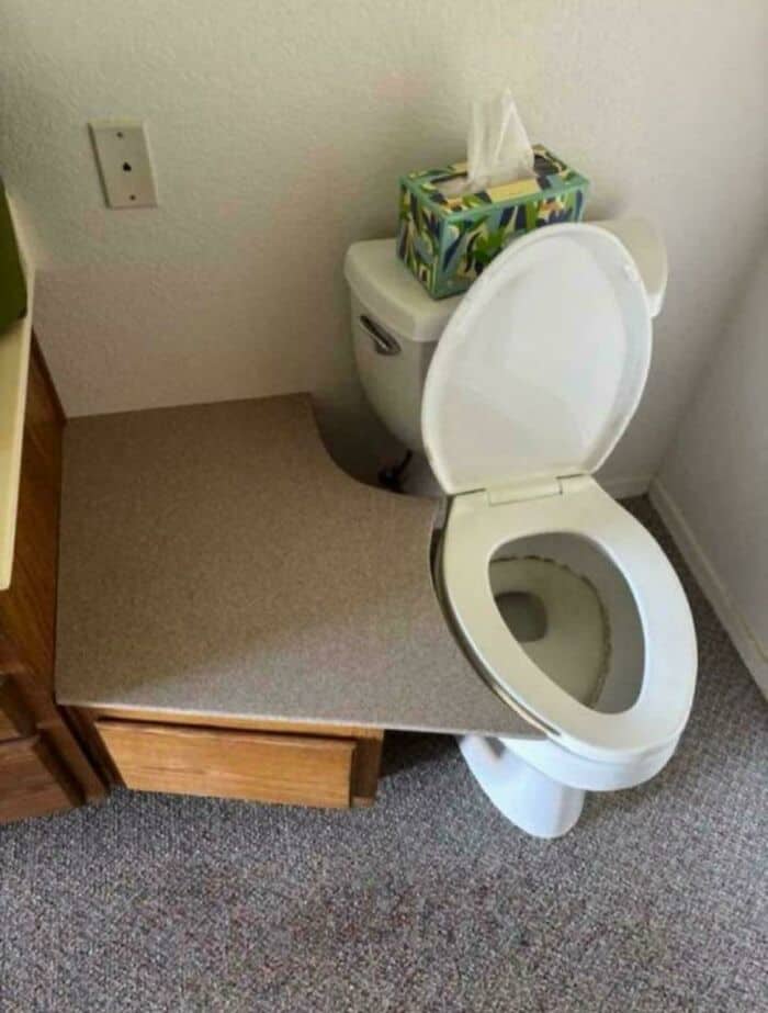 Toilet with tissue box on top, next to a wall outlet, in a small room.