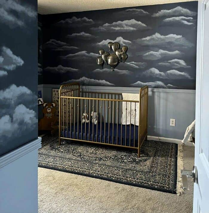 A baby crib in a room with cloud-themed wall art and a chandelier of balloons.