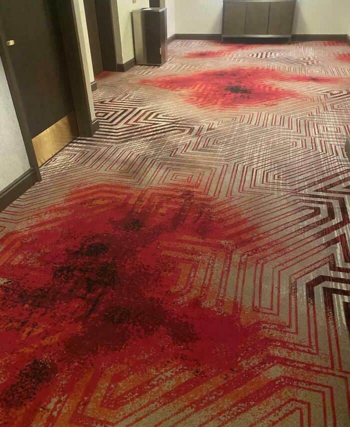 Carpet with red and black stains and geometric pattern in hallway.