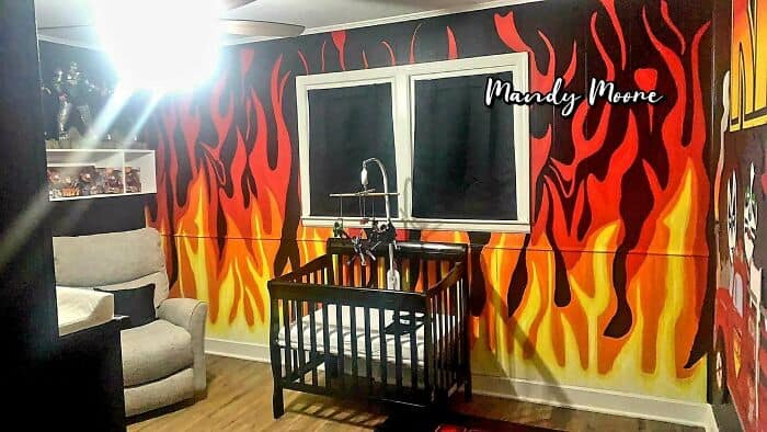 Fire-themed wall mural with flames in red, orange, and yellow, a window, and a black crib in a room.