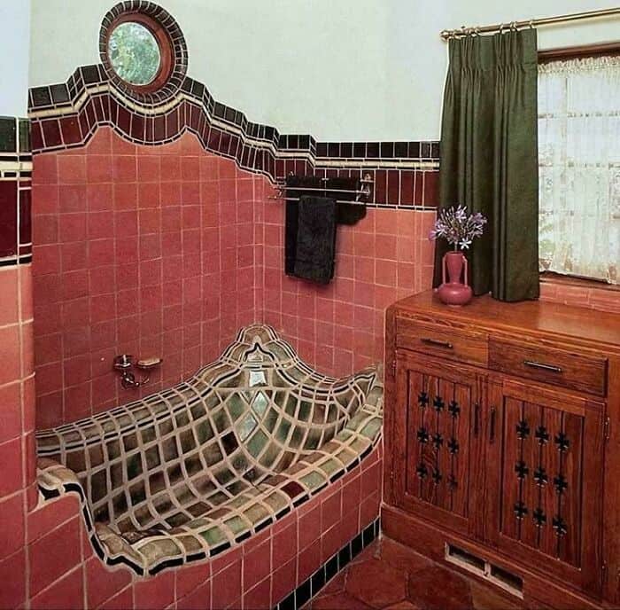 Vintage bathroom with a tiled bathtub and wooden cabinet, green curtains, and a small round window.