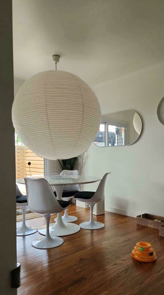 Round paper lantern hanging from ceiling in modern dining room with white chairs and wooden floor.