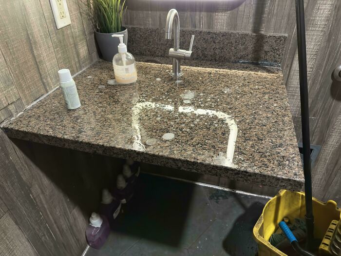 Granite bathroom countertop with sink, soap dispenser, and cleaning supplies.