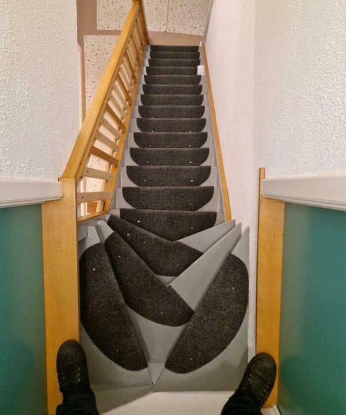 Broken staircase with black carpeted steps and wooden handrails.