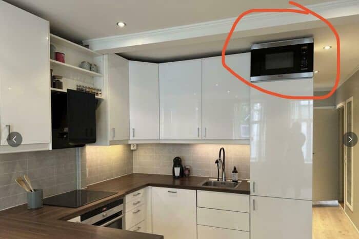 Modern kitchen with white cabinets, wooden countertop, and a microwave oven in the upper right corne.