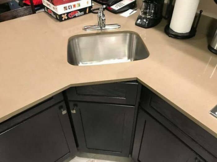 A stainless steel kitchen sink with a faucet on a beige countertop.