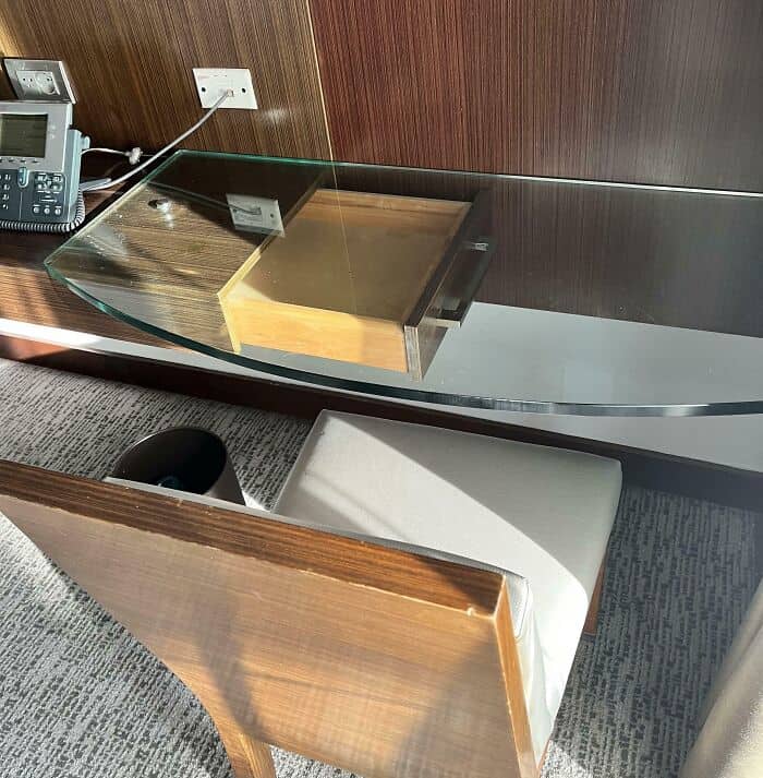 Desk with a glass top, wooden drawer, and a chair in an office setting.