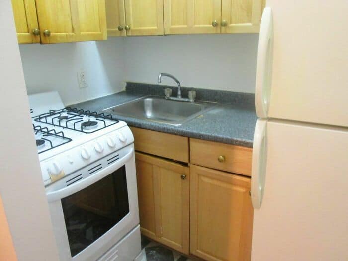 A compact kitchen corner with a stove, sink, and wooden cabinets.