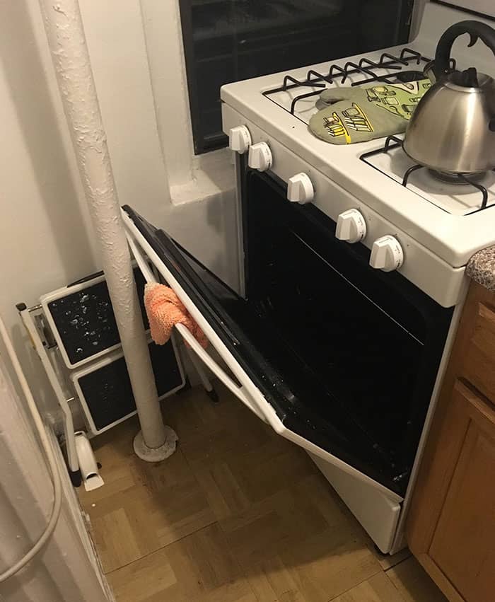 Stove with kettle and oven mitts in a small kitchen corner.