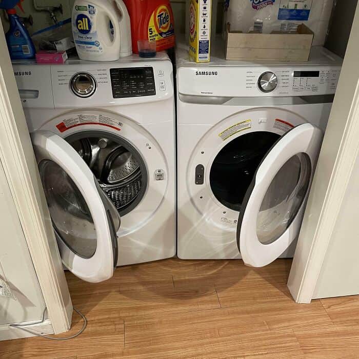 Washing machines side by side in laundry room with laundry supplies on top.