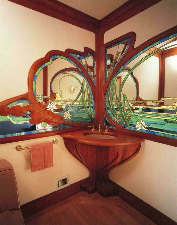 Artistic stained glass mirror with floral and abstract design in a corner bathroom.