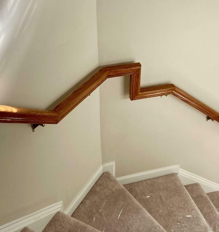 Handrail on beige staircase with white baseboards and wall corner.