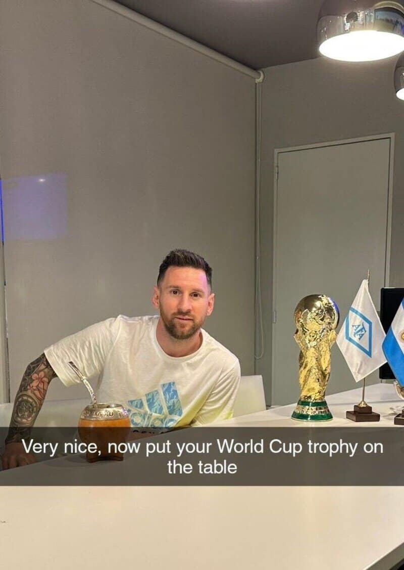 Man with tattoos sitting at a table with World Cup trophy and flags.