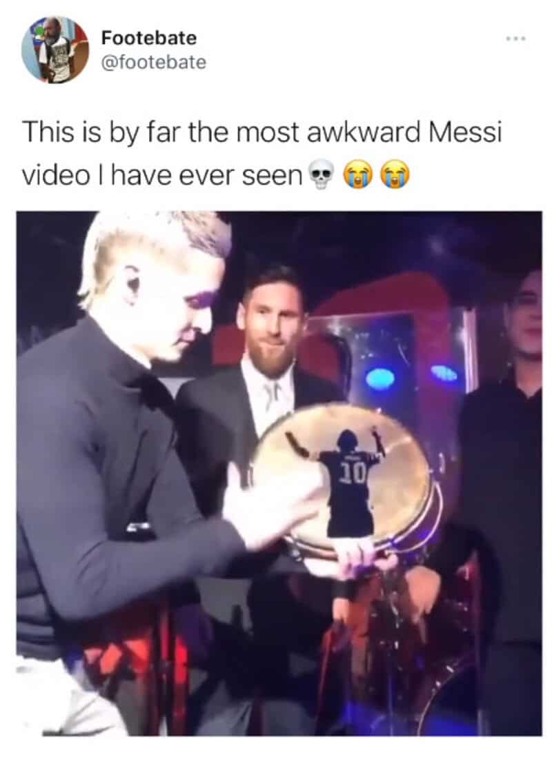 Messi holding a trophy with a person in a black suit in the background.