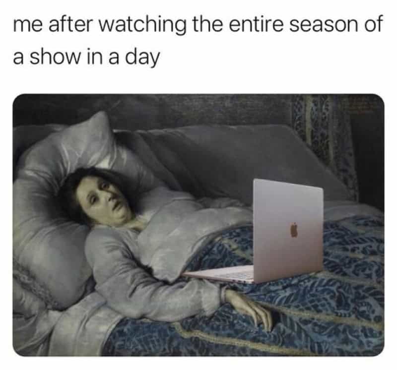 Woman lying in bed with a laptop, looking tired after binge-watching.