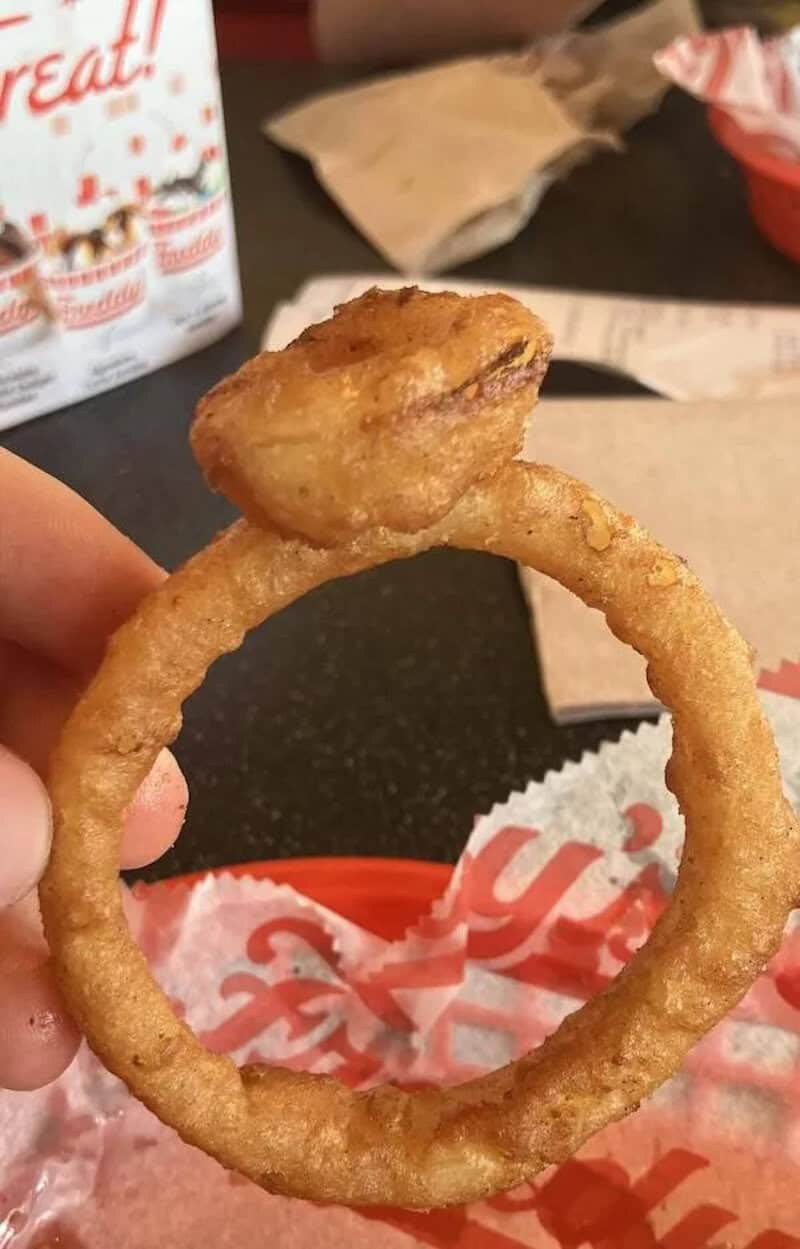 Fried onion ring with a small piece of chicken on top.