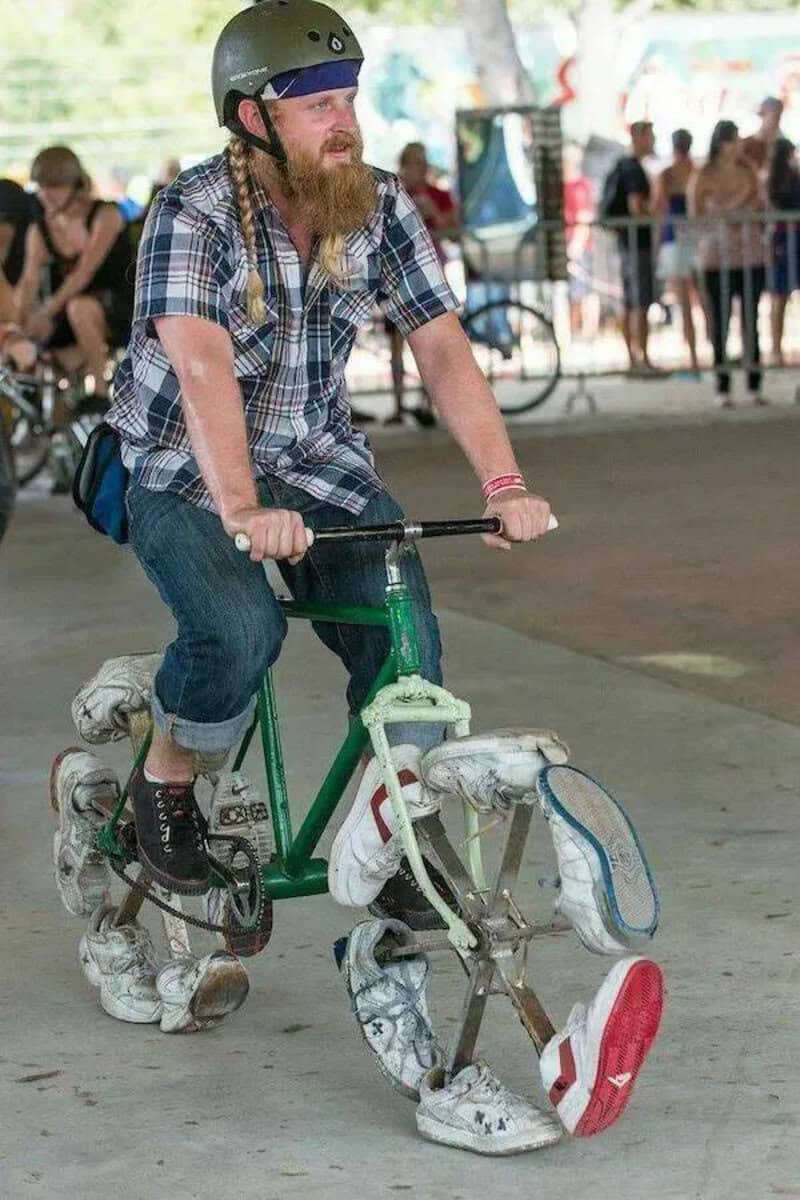 A man with a beard and long hair riding a bicycle with rollerblades attached to the wheels.