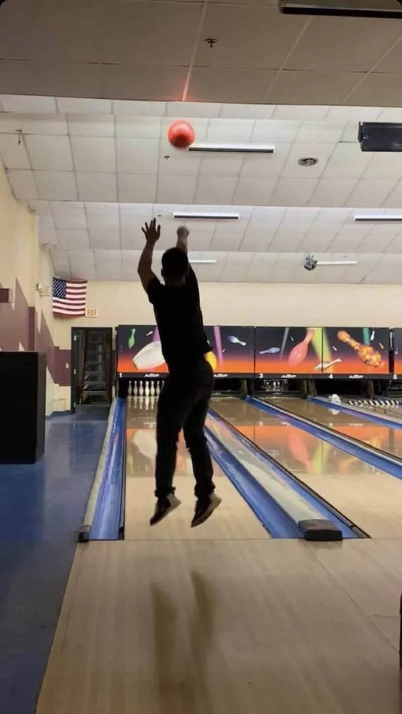 Ball in the air at bowling alley with person jumping to hit it.