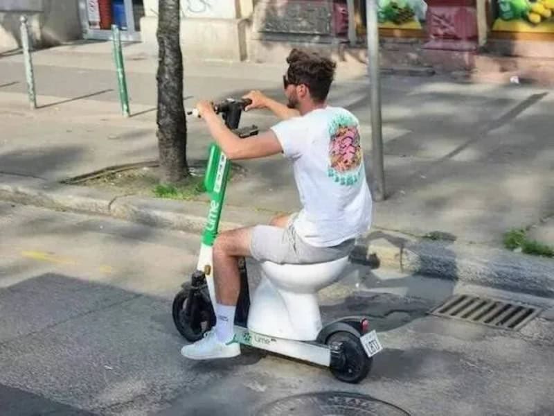 Man riding an electric scooter on a city street, sitting on a toilet.