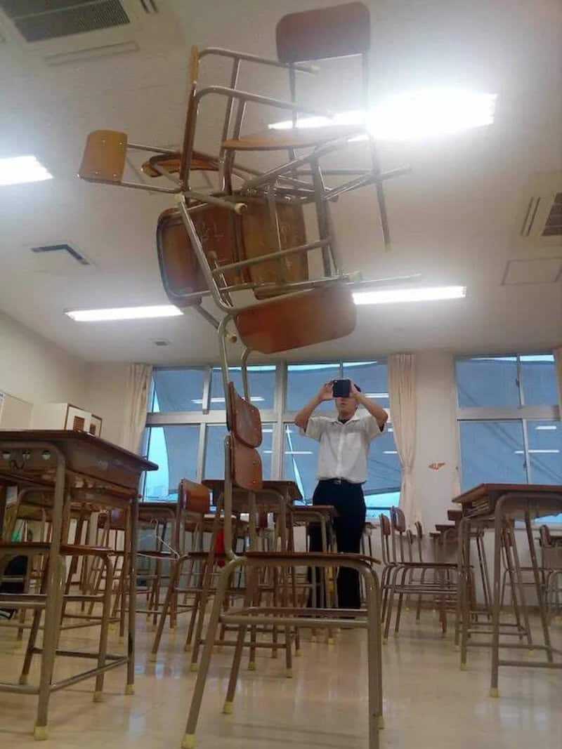Chairs stacked and floating in a classroom with a person taking a photo.