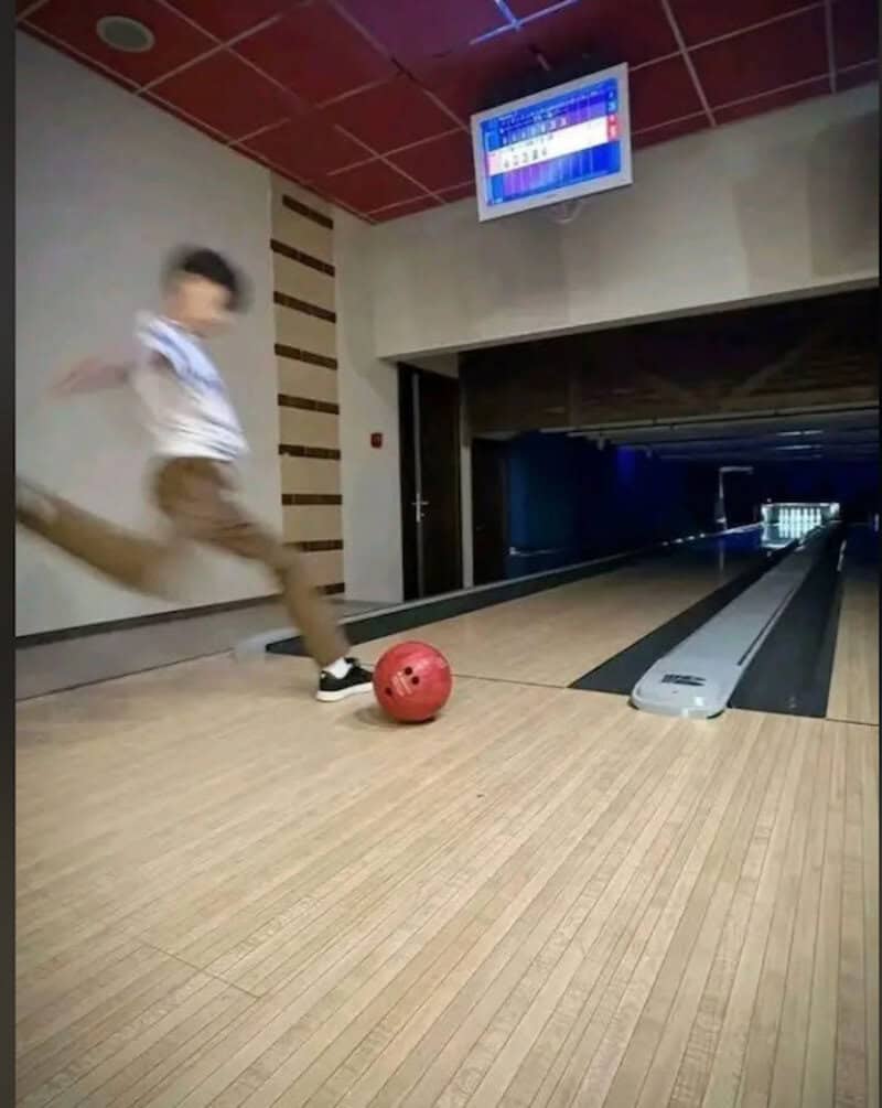 Child in motion at bowling alley with red ball, approaching the lane.