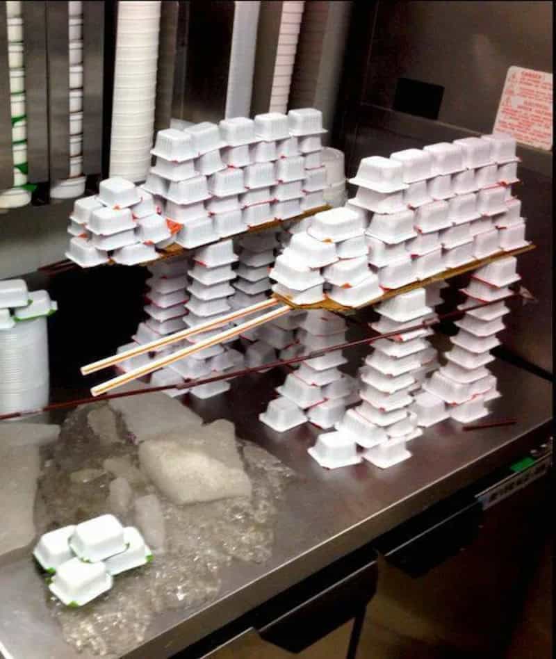 Stacked foam food containers on a stainless steel surface with chopsticks and ice.