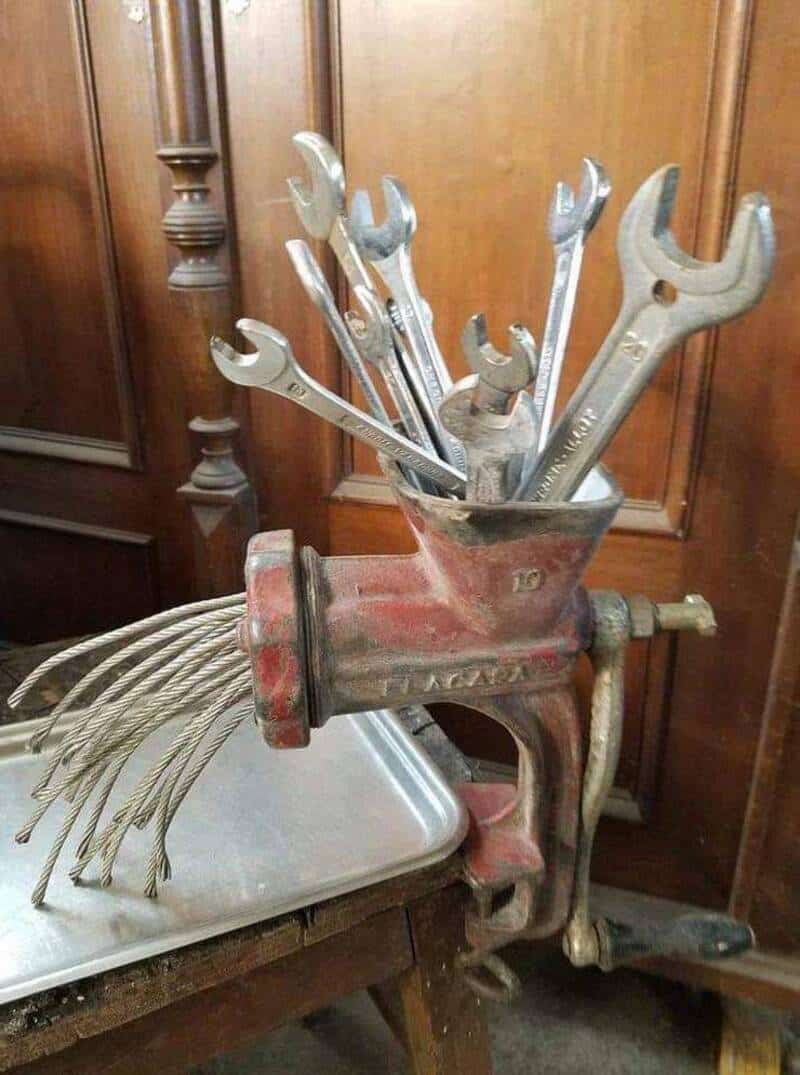 Wrench and pliers in a red vice clamp on a wooden workbench.