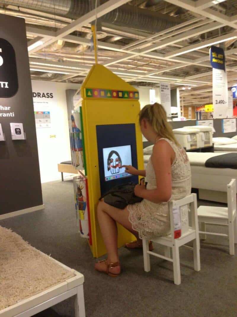 A woman sitting on a white chair using a touchscreen kiosk in a store.