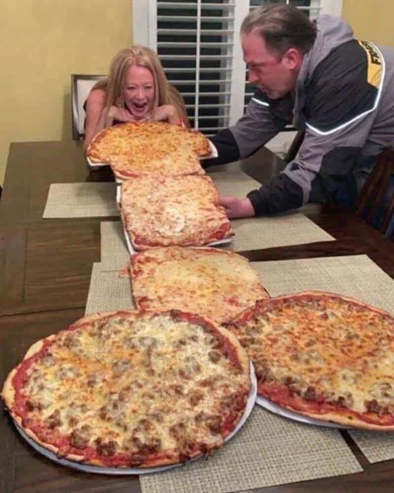 Girl excitedly reaching for large pizza with man at dinner table.