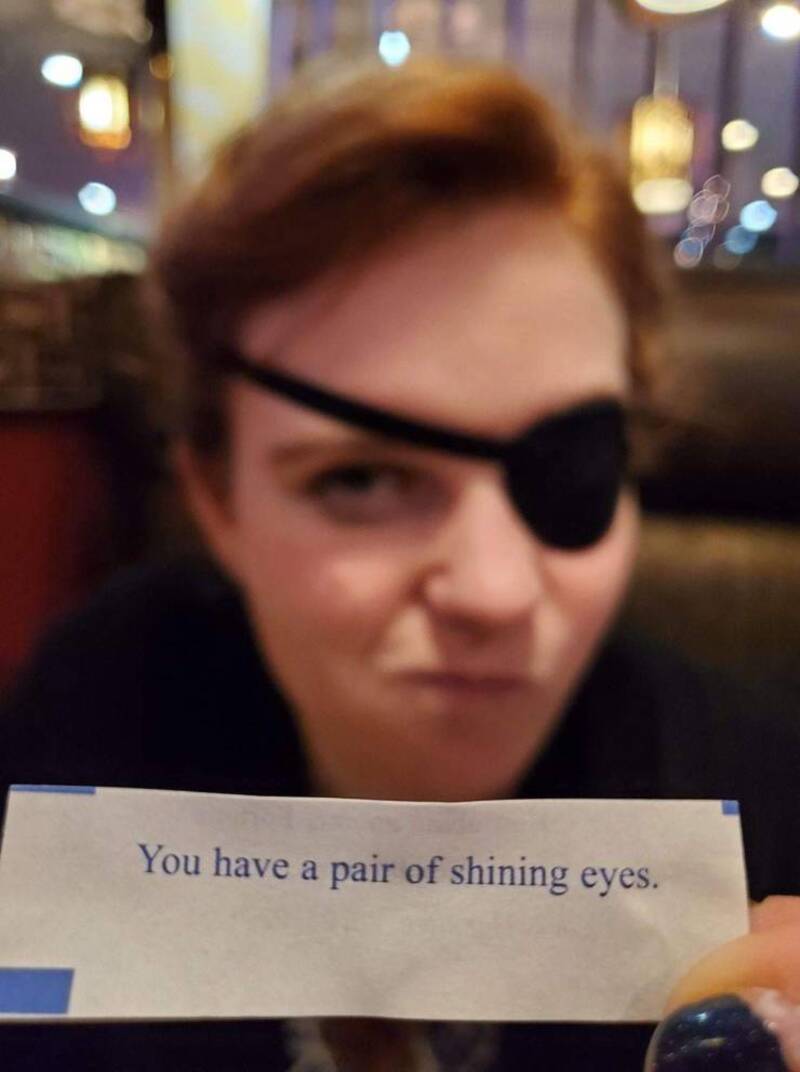 A woman with an eye patch holding a sign that says "You have a pair of shining eyes.".