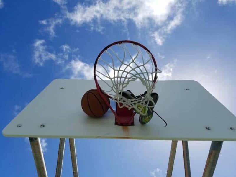 Basketball hoop with a ball and a pair of sneakers on a white table against a blue sky with clouds.