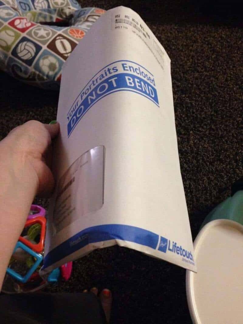 Person holding a rolled-up document with "Portraits Enclosed" and "DO NOT BEND" text.