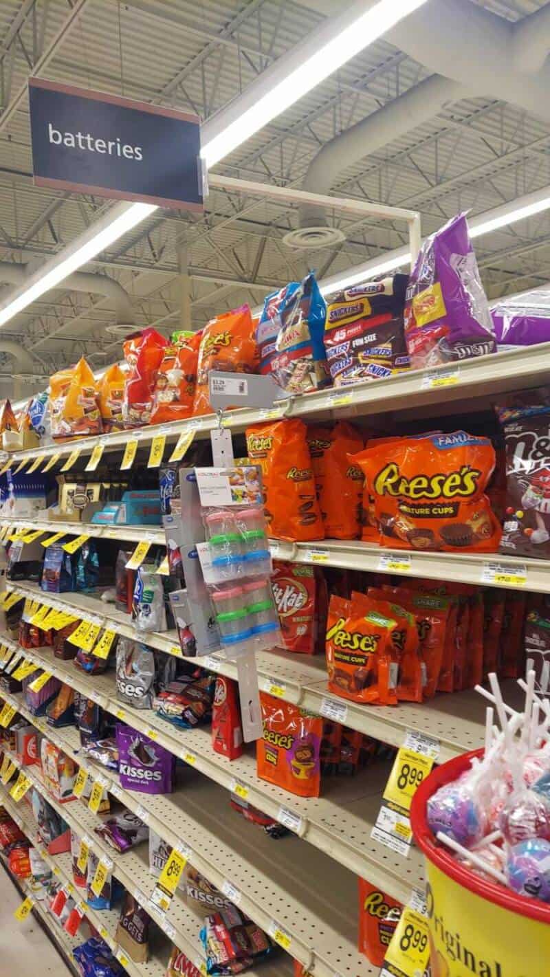 Assorted bags of Reese's and other candies on store shelves under a "batteries" sign.