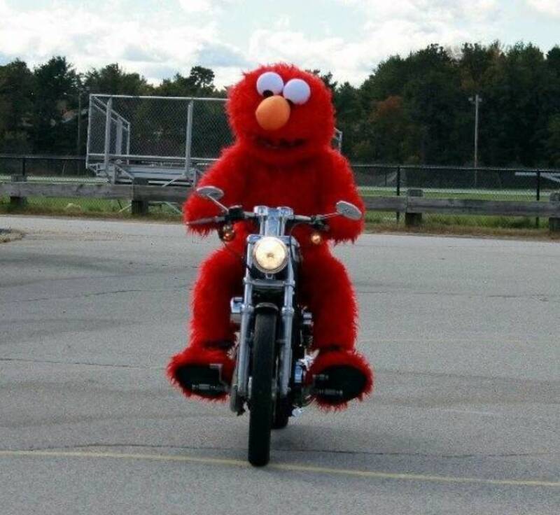Elmo riding a motorcycle on an empty parking lot.