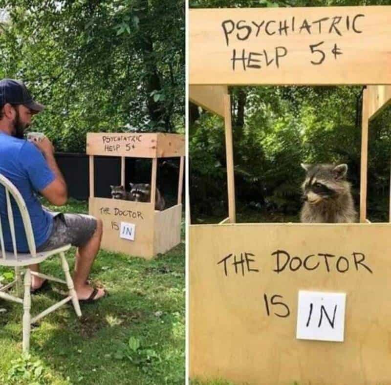 A man sitting on a chair at a homemade "psychiatric help" booth with a raccoon inside.
